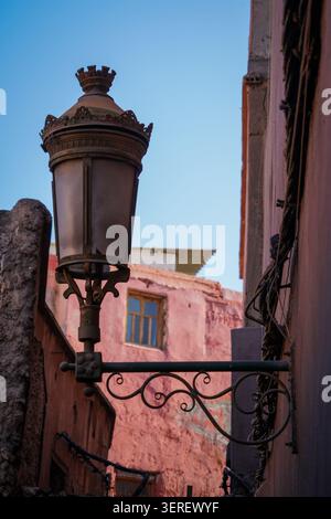 A detailed view of an ornate, vintage street lamp, featuring intricate scrollwork and a crown-like finial, mounted on a weathered, textured pink build Stock Photo
