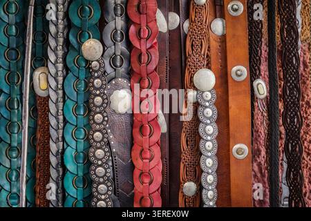 A close-up vertical shot displays a vibrant collection of handcrafted leather belts, showcasing various textures, colors, and designs. The belts featu Stock Photo