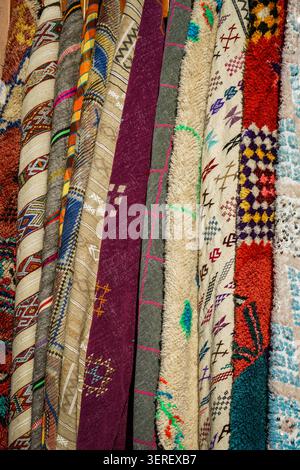 A close-up vertical view of an assorted collection of colorful Moroccan rugs and carpets hanging together. Each rug features unique hand-woven traditi Stock Photo