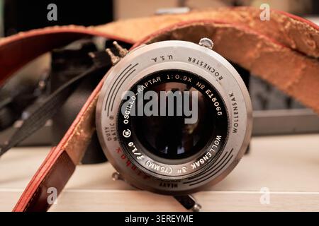 Modern digital body fitted with an old manual prime lens and a rustic leather strap on a desk next to a dark keyboard under warm room light. Stock Photo
