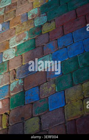 A full-frame, high-angle shot captures a textured surface of old brick pavement, with individual bricks painted in various faded and chipped colors. M Stock Photo
