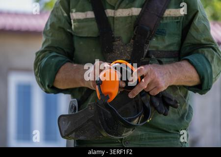 Worker holding a protective face shield with hearing protection before operating a brush cutter. The image highlights personal protective equipment, w Stock Photo