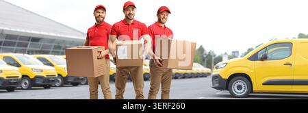 Delivery men holding boxes in front of a fleet of yellow vans Stock Photo