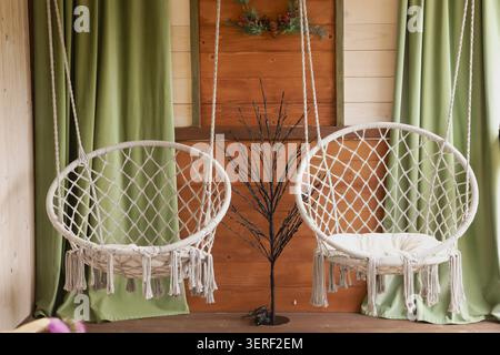 Cozy Hanging Macrame Chairs in Rustic Wooden Cabin Interior with Green Curtains Stock Photo
