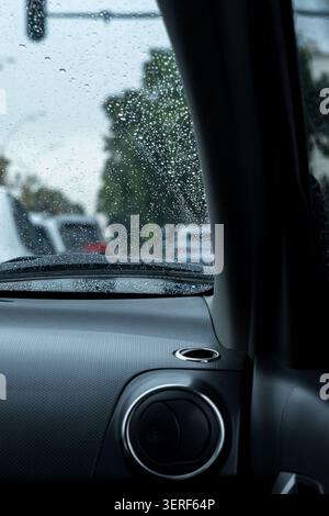 Raindrops on a car windshield viewed from the inside dashboard area. Concept: Promoting safe driving practices, caution, and vehicle interior comfort Stock Photo