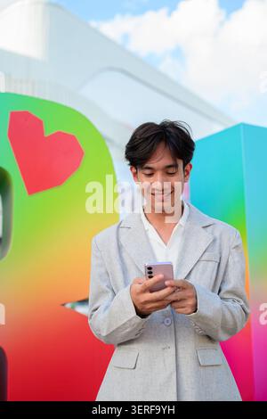 Vertical medium shot of a young nonbinary gender fluid Thai Isan businessman wearing a smart casual gray blazer and white shirt. Standing outdoors aga Stock Photo