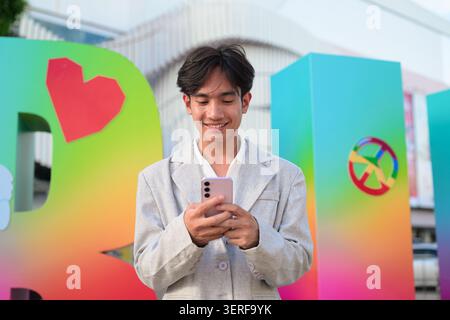 Horizontal medium shot of a young nonbinary gender fluid Thai Isan businessman dressed in a smart casual gray blazer and white shirt. He stands outdoo Stock Photo