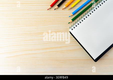 Colored pencils next to a blank spiral notebook on a wooden desk. A minimalist flat lay composition representing education, art, and creativity. Stock Photo