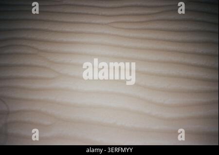 A flat, straight-down close-up of a wind-rippled desert sand surface, showing fine parallel wave patterns formed by aeolian processes. The near-unifor Stock Photo