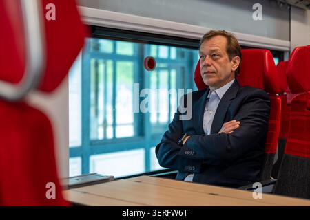 Middle aged man sits in a train carriage with folded arms Stock Photo