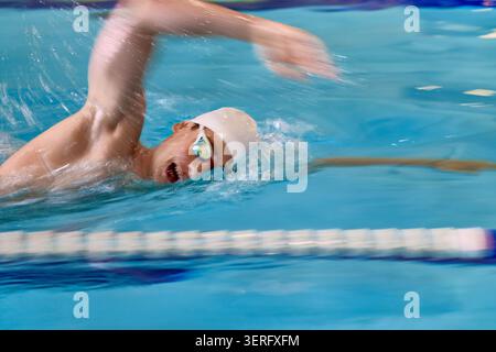 Swimmer moving fast through pool water with blurred freestyle stroke. Stock Photo