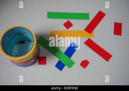 Stacked colorful adhesive tape rolls next to abstract geometric strips on white background Stock Photo