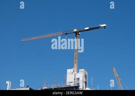 Construction cranes stand over a high-rise work site. Yellow tower crane and mobile crane against a blue sky Stock Photo