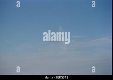A solitary dark lenticular cloud floats against a vast blue sky with wispy cirrus clouds, creating a mysterious and surreal atmosphere. Stock Photo