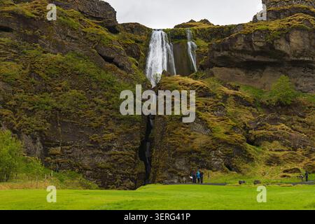 Low-angle view of the iconic Seljalandsfoss waterfall cascading down a high cliff under a dramatic overcast sky in Iceland. Stock Photo