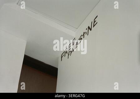 Upward-angle view of a white wall corner with a bold political message written in dark lettering near the ceiling. Stark indoor setting with a doorway Stock Photo