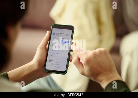 Close up of man using smartphone, planning route with travel app in hotel for family vacation. Supporting booking, trip planning, hospitality marketing, mobile tourism services Stock Photo