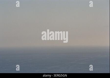 A minimalist seascape showing a calm ocean merging with a hazy, fog-filled sky. Soft muted tones create a serene, melancholic atmosphere. Stock Photo
