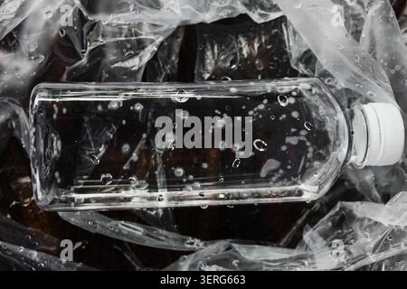 Clear Plastic Water Bottle with Droplets Lying on Crumpled Cellophane Sheet Stock Photo