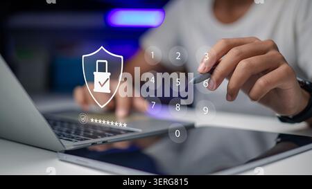 Hand using stylus pen on virtual numeric keypad for cybersecurity login on laptop and tablet, double exposure with padlock shield icon for data protec Stock Photo