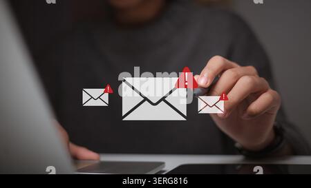 Hand using stylus pen pointing at virtual email icon with red warning alert sign on laptop, concept of cybersecurity breach, spam mail, phishing attac Stock Photo