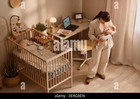 Adult Mother Holding Baby While Working from Home in Nursery Stock Photo