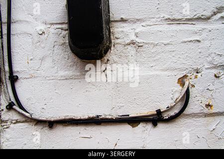 A dirty old white painted brick wall with a key box fitted and aged electrical cables fixed to the wall. Stock Photo