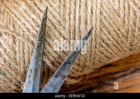 Twine roll, a natural coarse string, resting on a textured wooden surface next to open metal scissors, preparing for craft, gardening, or packaging ta Stock Photo
