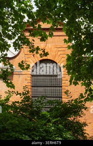 Lush trees frame a red brick window of St Anne & St Agnes Church, City of London Stock Photo