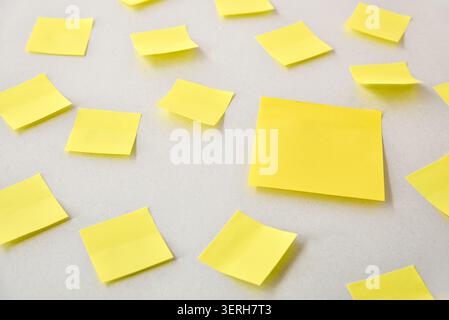 Multiple yellow sticky notes scattered across a clean white surface, creating a minimal office organization and brainstorming concept with ample copy Stock Photo