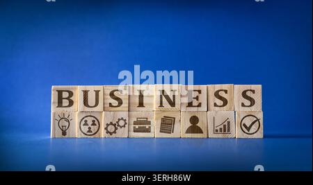 Wooden blocks spell BUSINESS with corporate icons below on a blue background, representing management, strategy, growth, innovation, and organizationa Stock Photo