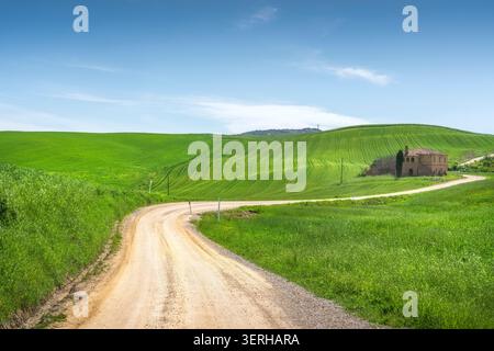 View of the historic Via Francigena dirt road winding through rolling hills with an old abandoned farmhouse near Torrenieri. Tuscany, Italy Stock Photo