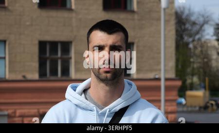 Portrait of young confident bearded man in casual clothing with cityscape background. Close up of handsome guy looks into camera standing at city Stock Photo