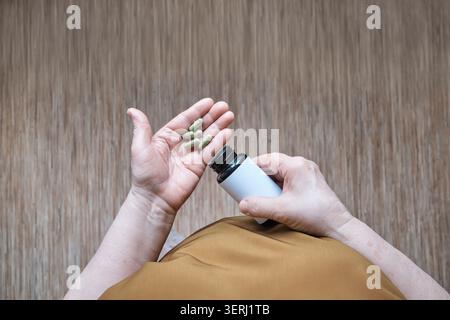 Senior woman hands pouring green herbal capsules into palm for wellness and treatment Stock Photo