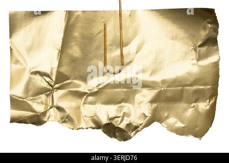 Crumpled gold foil paper piece hanging on paperclip, isolated on white background. Stock Photo