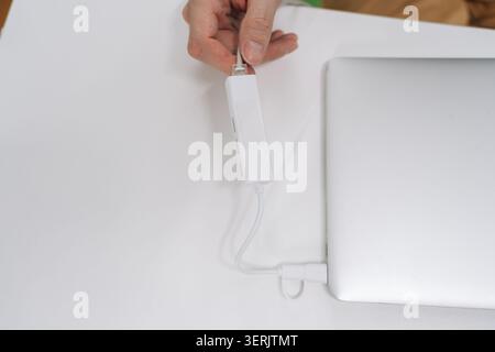 Hand inserting ethernet cable into USB c hub connected to laptop on white desk, upgrading to wired high speed network connectivity for office or home Stock Photo