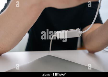 Close-up shot of person in black shirt at white desk holding multiport USB adapter. Shallow depth of field focuses on technology gadget. Modern, clean Stock Photo