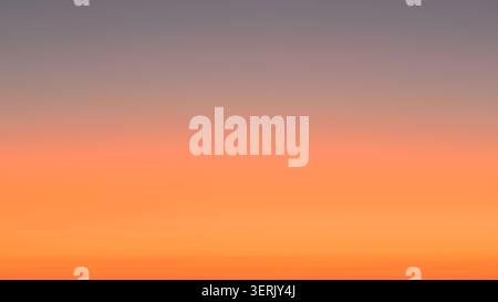 Sunset over the ocean with colours fading from reddish-orange to grey. Stock Photo