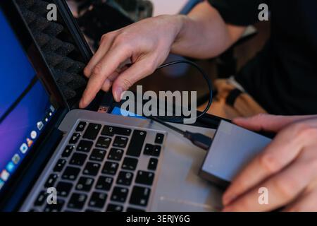 Person hands connecting USB cable from external hard drive to laptop, facilitating data transfer and storage backup for important digital information Stock Photo
