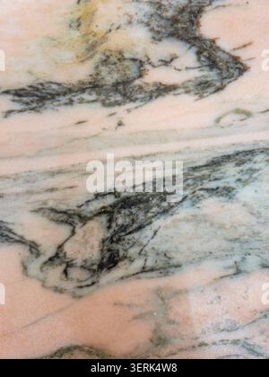 A polished natural marble surface with shades of dark green and black minerals set in a soft peach pink stone. The texture highlights unique patterns Stock Photo
