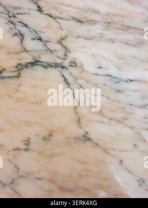 Beige marble with elegant grey and charcoal veins running across it. The polished stone reflects light in a smooth texture throughout the area. Stock Photo