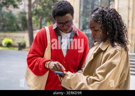 Focused african american couple man and woman friends discussing and watching media on smartphone. Stock Photo