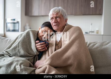 Senior family man and woman sharing cold flu sickness, sitting together on sofa suffering from fever Stock Photo