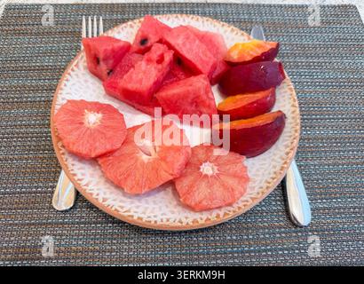 Fresh sliced watermelon grapefruit and plum arranged on ceramic plate with utensils Stock Photo