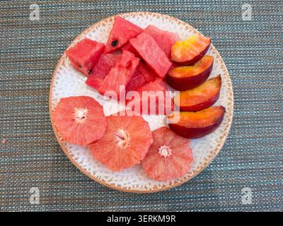 Top-down plate of sliced grapefruit watermelon and nectarine on woven placemat bright summer snack Stock Photo