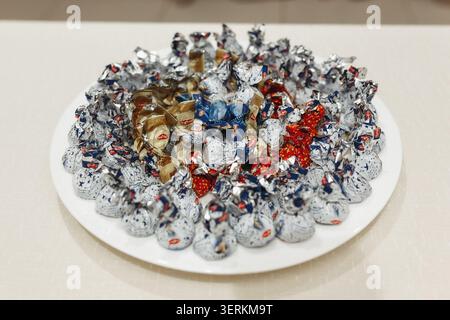 Shiny foil-wrapped candies cluster on a white plate. Colorful wrappers gleam under soft, even lighting. Red, gold, and blue hues add festive appeal Stock Photo