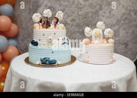 Sweet cakes adorned with playful figures and soft pastel tones. Pastel balloons add cheerful background texture. Cakes sit on white tablecloth with el Stock Photo