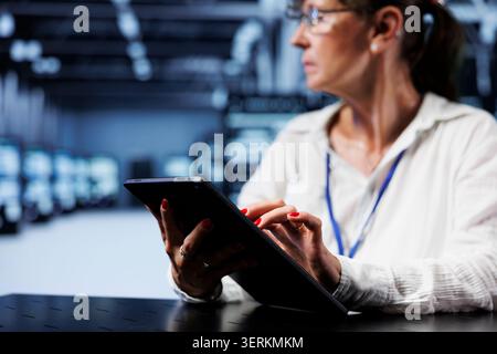 Trained serviceman using tablet to assess server security blips arising due to unsecured network connections. Qualified repairman ensuring data center is impenetrable by malware attacks. Stock Photo
