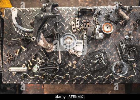 A collection of disassembled car engine components and fasteners are neatly arranged on a diamond plate workbench, ready for repair or maintenance Stock Photo