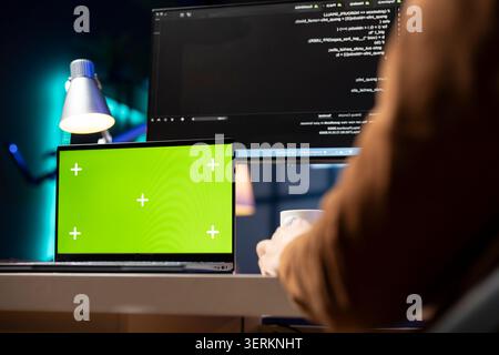 Man working from home using isolated screen laptop, testing and deploying programs and systems. Programmer checking code displayed on computer monitors using chroma key notebook. Stock Photo